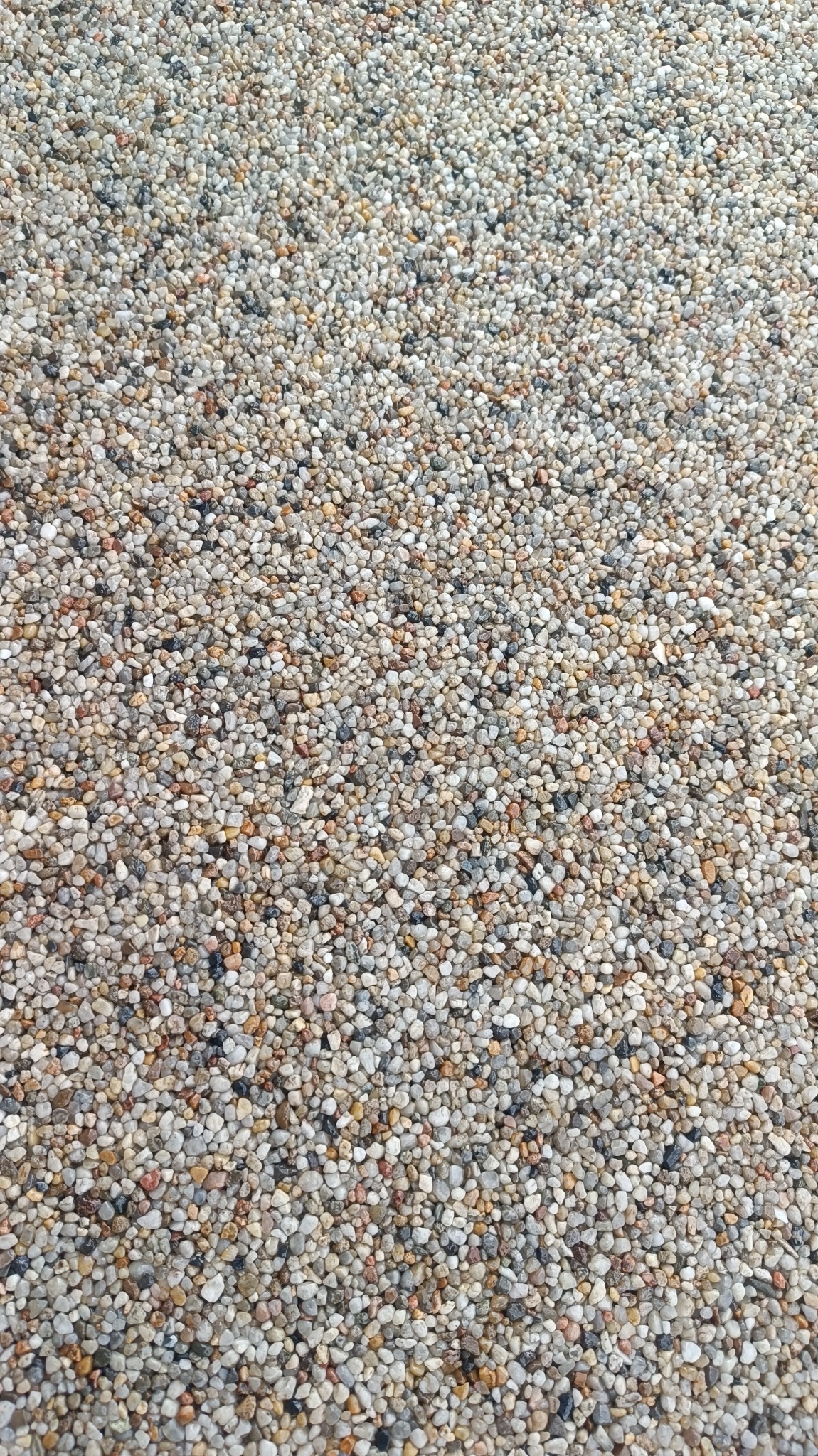 Beżowo-szara posadzka z drobnych kamyczków, tworząca wzór 'kamiennego dywanu', z widocznymi różnicami w odcieniach i fakturze poszczególnych kamieni.