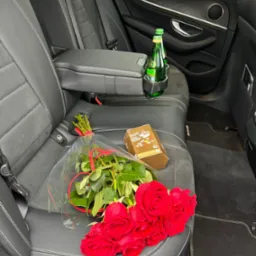 Luksusowy przewóz: bukiet czerwonych róż, słodycze i woda mineralna na tylnym siedzeniu czarnego, skórzanego auta Mercedes, gotowe na specjalną okazję.