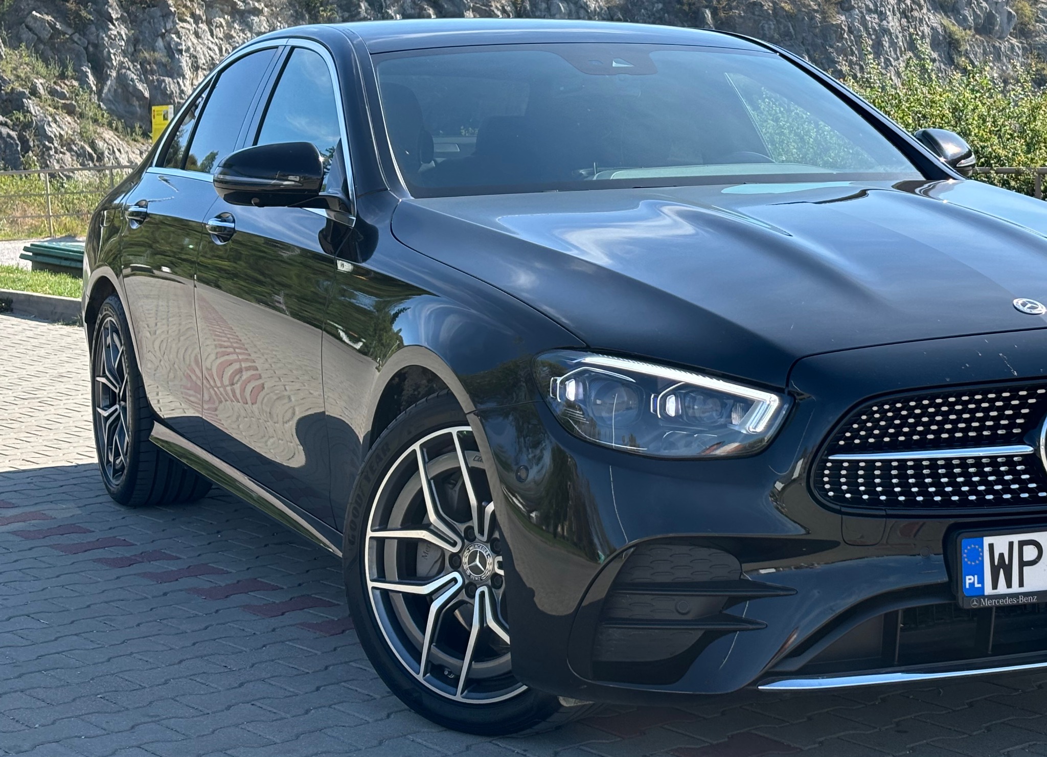 Czarny Mercedes-Benz klasy E na brukowanej powierzchni z górą w tle.