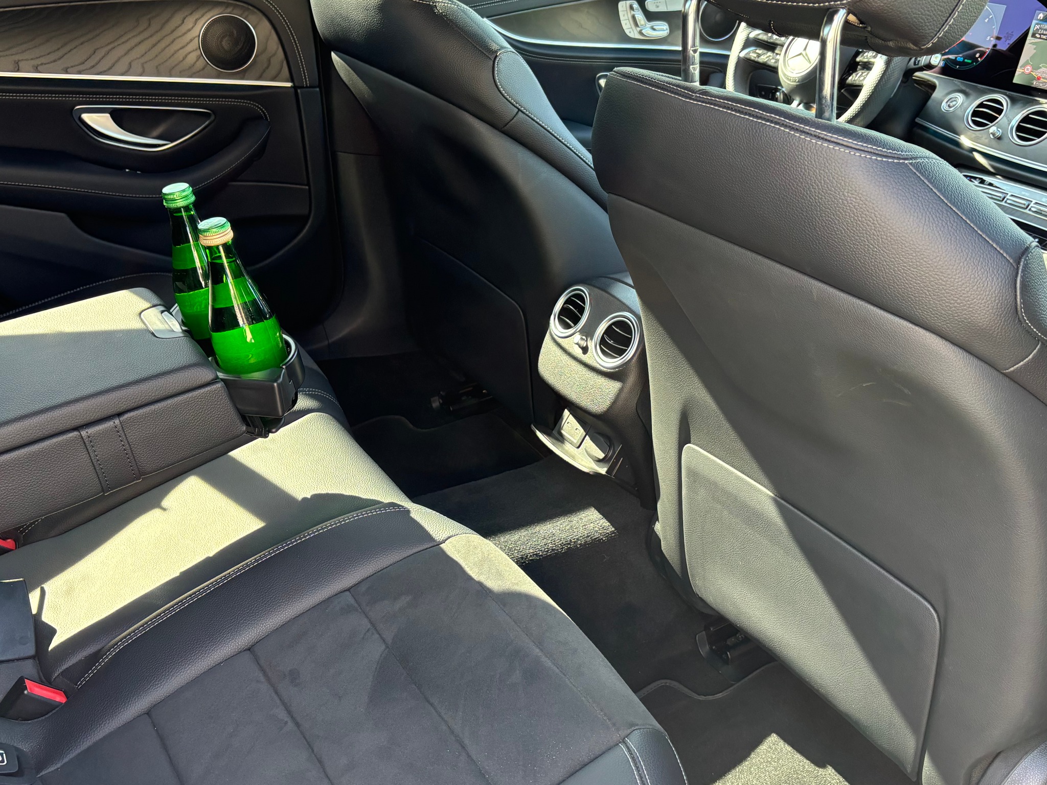 Wnętrze luksusowego samochodu z czarną skórzaną tapicerką, widoczne dwie butelki zielonej wody w uchwycie na napoje na tylnym siedzeniu