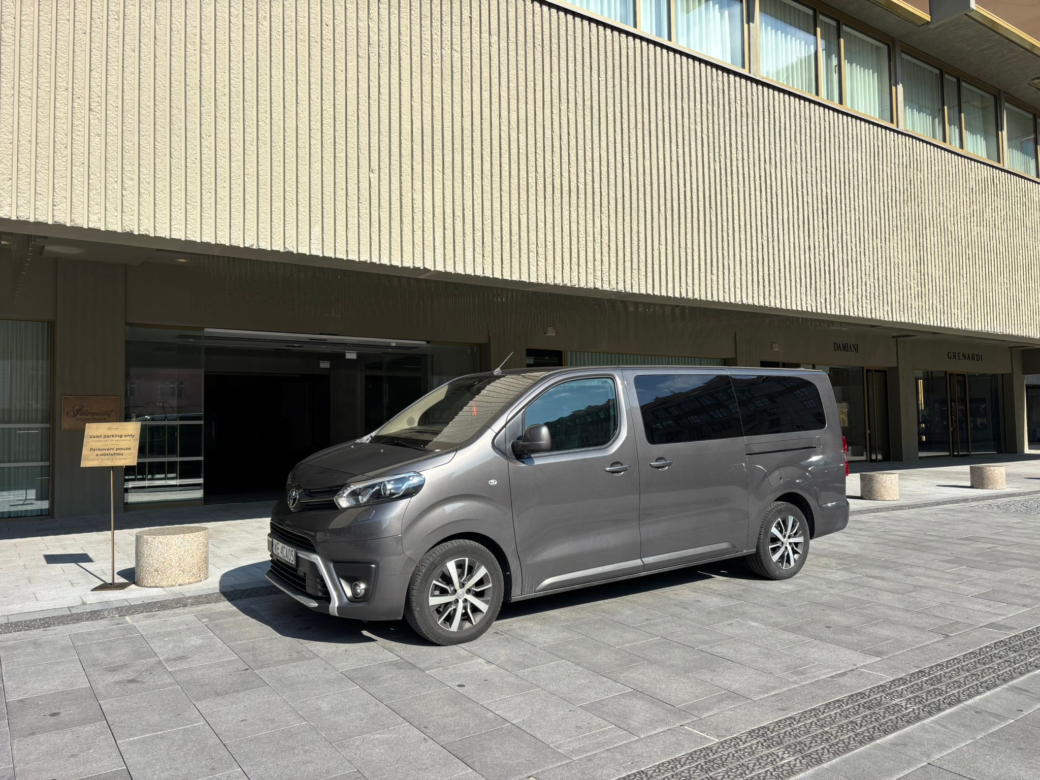 Szary, nowoczesny van Toyota Proace Verso zaparkowany przed budynkiem Fairmont Golden Prague. Tablica informacyjna 'Valet parking only'.
