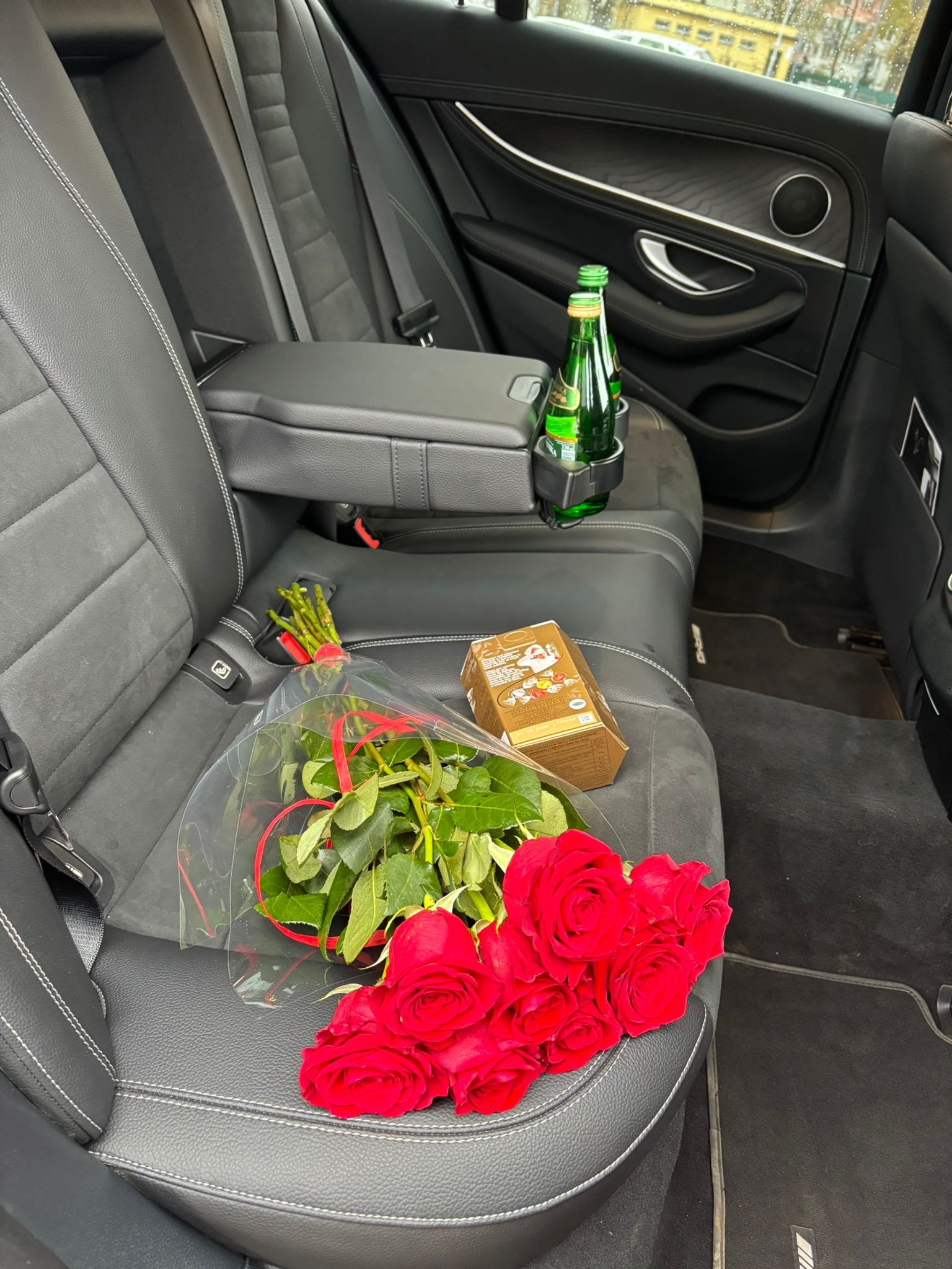 Luksusowy przewóz: bukiet czerwonych róż, słodycze i woda mineralna na tylnym siedzeniu czarnego, skórzanego auta Mercedes, gotowe na specjalną okazję.