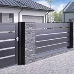 Nowoczesna brama przesuwna w kolorze antracytowym z poziomymi, srebrnymi akcentami, osadzona na słupkach wykończonych kamieniem dekoracyjnym, na tle domu z garażem i chodnika z kostki.