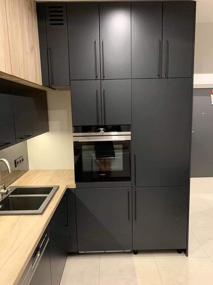 Nowoczesna, grafitowa zabudowa kuchenna z piekarnikiem Siemens, jasny blat i płytki. Minimalistyczne uchwyty, gładkie fronty szafek, oświetlenie podszafkowe.