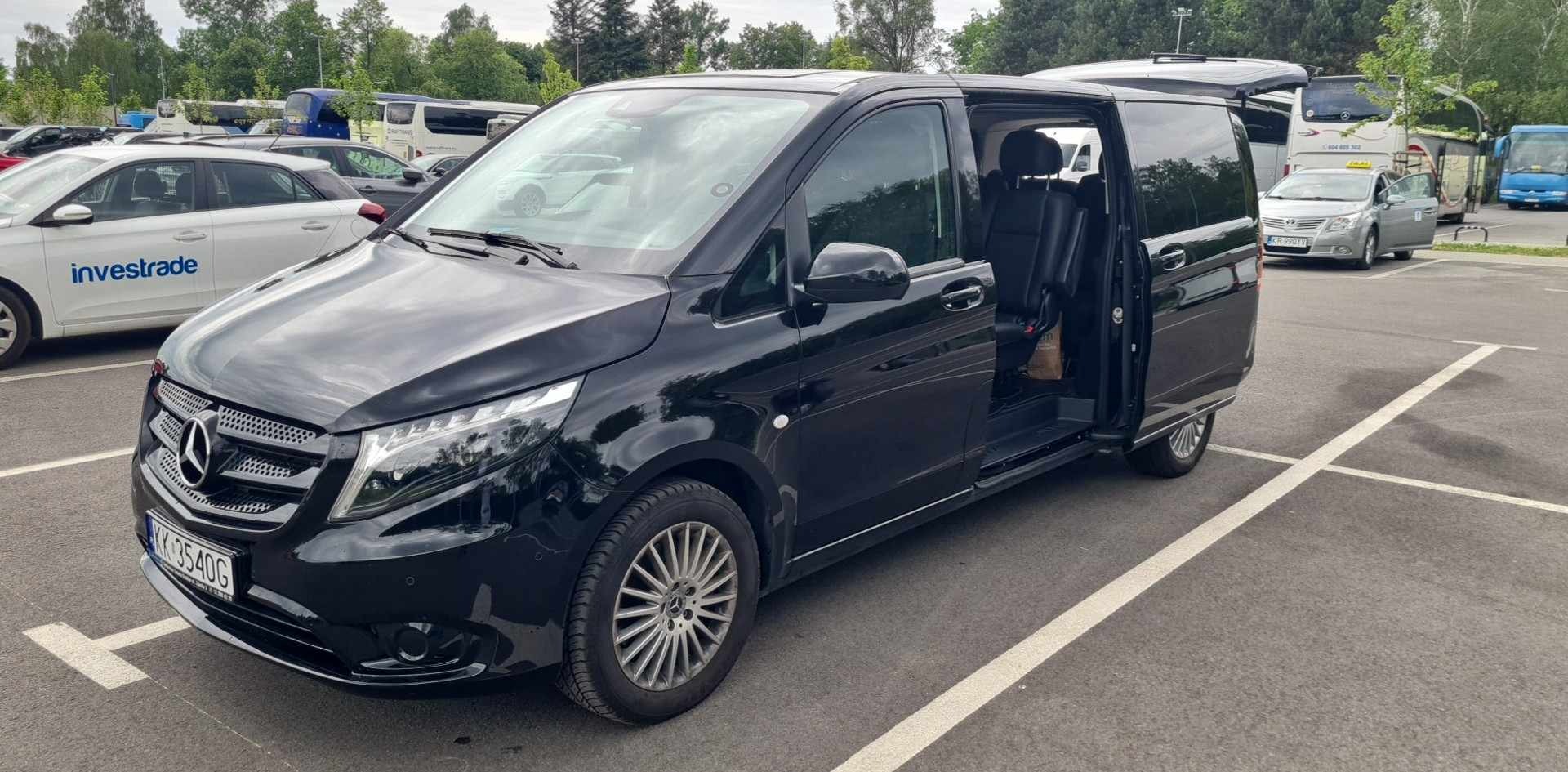 Czarny, luksusowy van Mercedes-Benz Vito z otwartymi drzwiami przesuwnymi na parkingu, widoczne skórzane fotele wewnątrz.