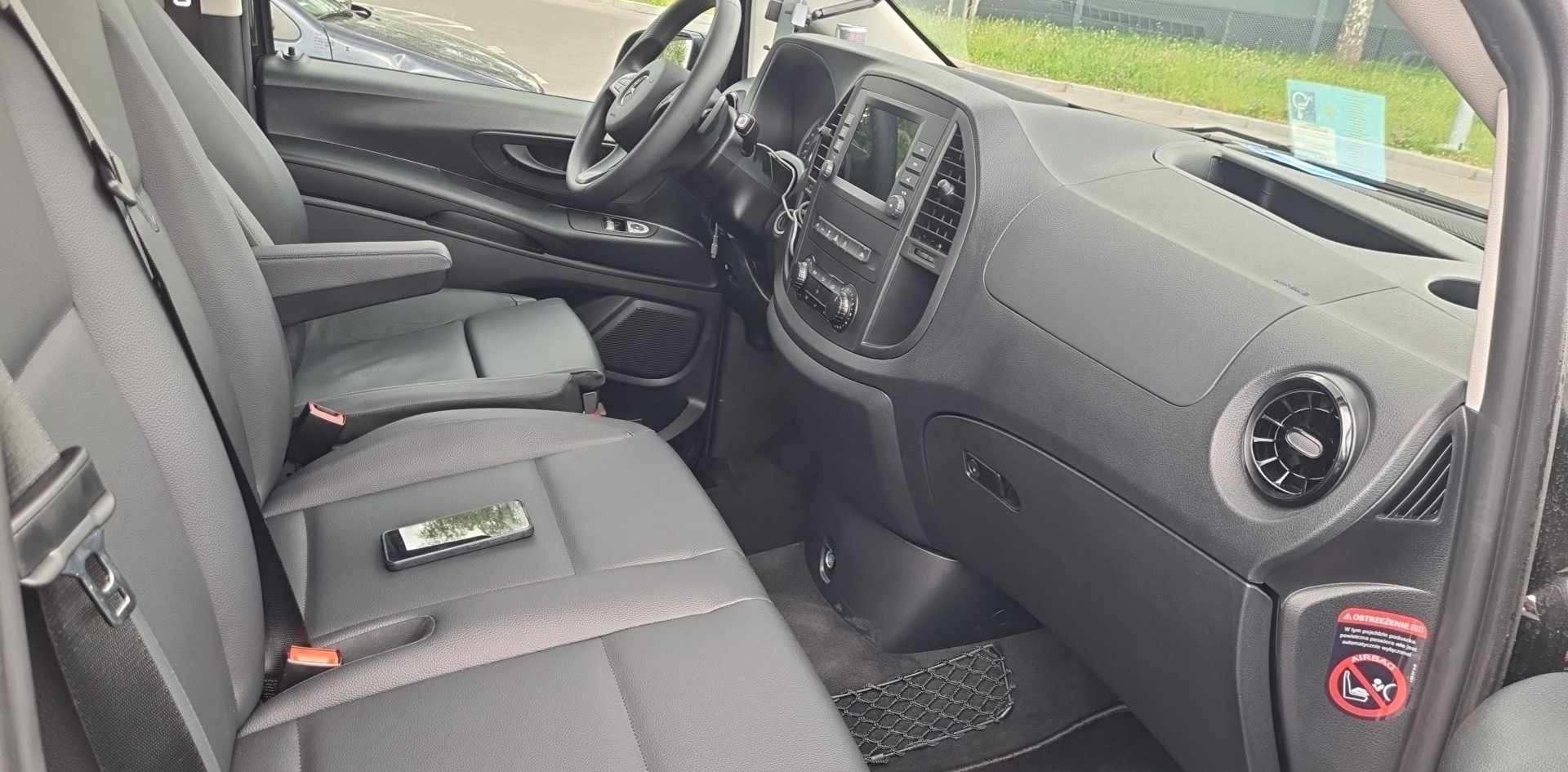 Wnętrze busa Mercedes Vito z czarną tapicerką, widok na przednie fotele i deskę rozdzielczą, telefon leżący na siedzeniu pasażera.