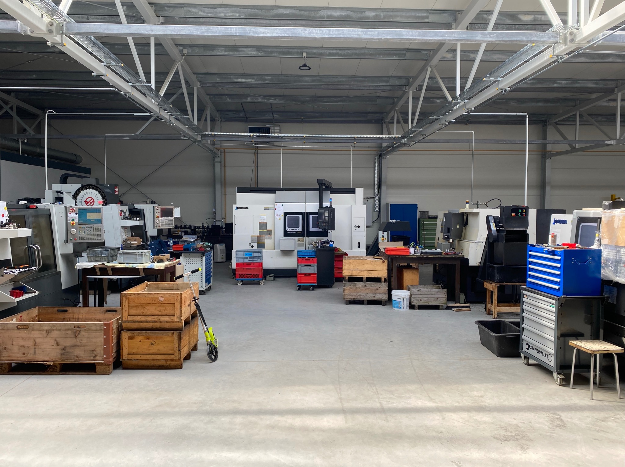 Przestronny warsztat obróbki metali z kilkoma frezarkami CNC i tokarkami, widoczne skrzynie narzędziowe i suwnica pod sufitem.