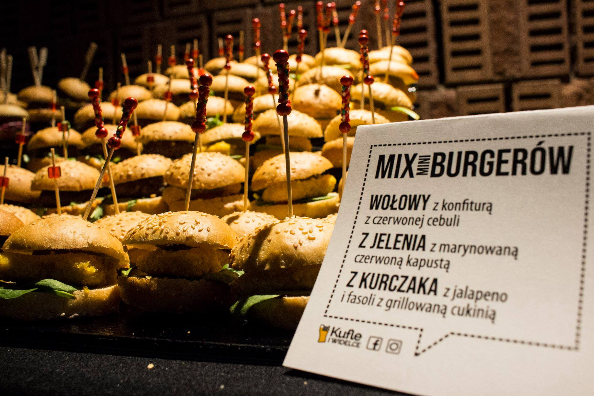 Mini burgery wołowe, z jelenia i kurczaka, ustawione warstwami na czarnym blacie, każdy z ozdobną wykałaczką; obok kartka z menu 'Mix Burgerów' z opisem składników.