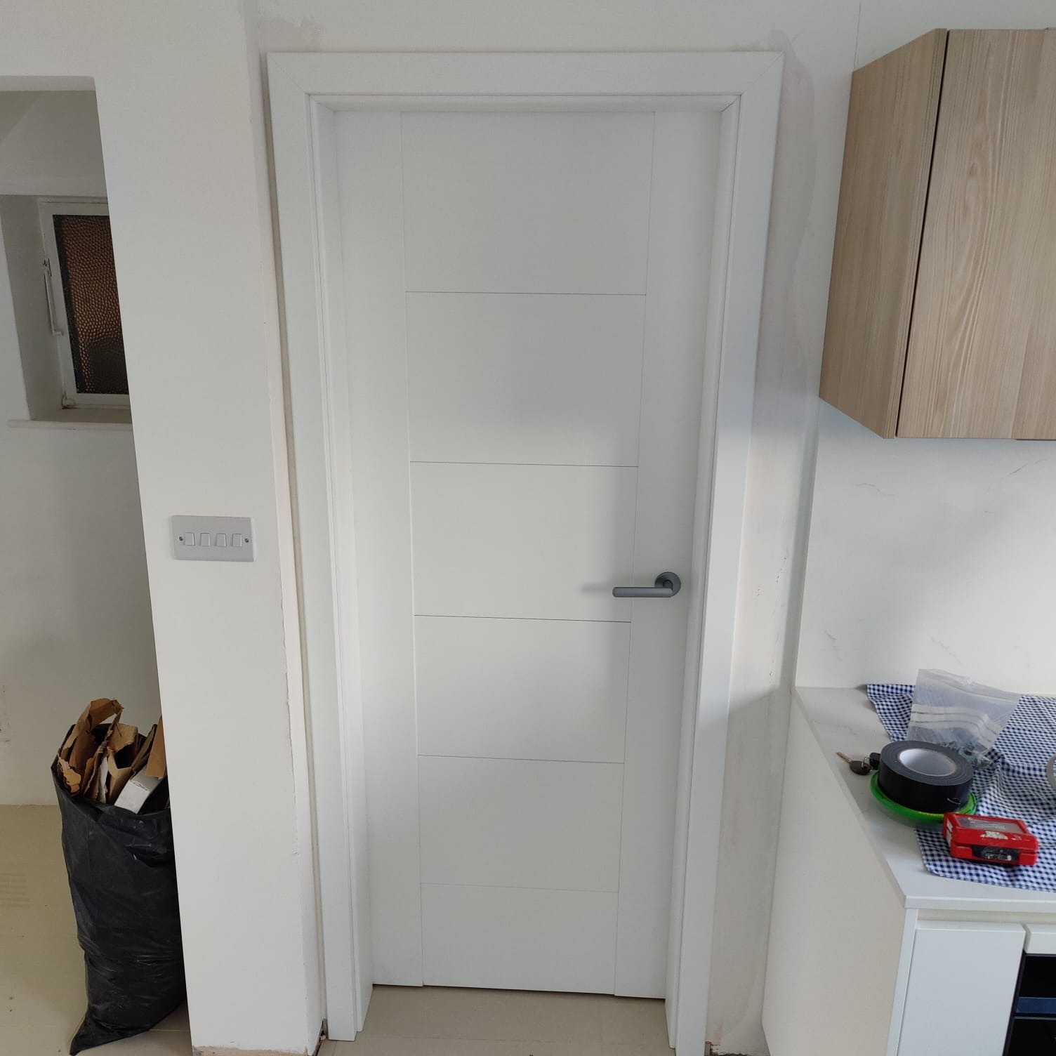 Białe drzwi wewnętrzne z czterema panelami, zamontowane w ościeżnicy, widoczne narzędzia i odpady budowlane w tle.