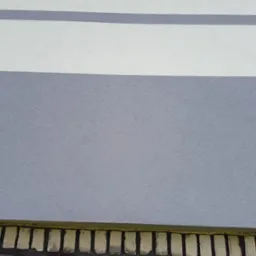 Fragment elewacji budynku z szarą i białą farbą w poziome pasy oraz ozdobnym elementem dekoracyjnym przy podstawie ściany.