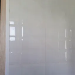 Ściana wyłożona jasnymi, błyszczącymi płytkami imitującymi marmur w Mężeninie, widoczny fragment drewnianej ościeżnicy drzwi.