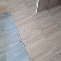 Złota rączka - Podłoga wyłożona dwoma rodzajami płytek imitujących drewno: jasnobrązowe i szare. Widoczny fragment ościeżnicy drzwi.