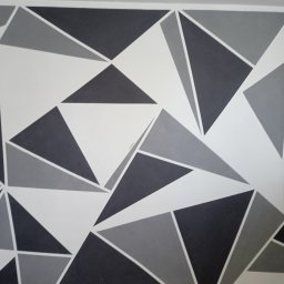 Złota rączka - Ściana pomalowana w geometryczny wzór z trójkątów w odcieniach szarości i bieli, tworząca nowoczesny i dynamiczny efekt wizualny.
