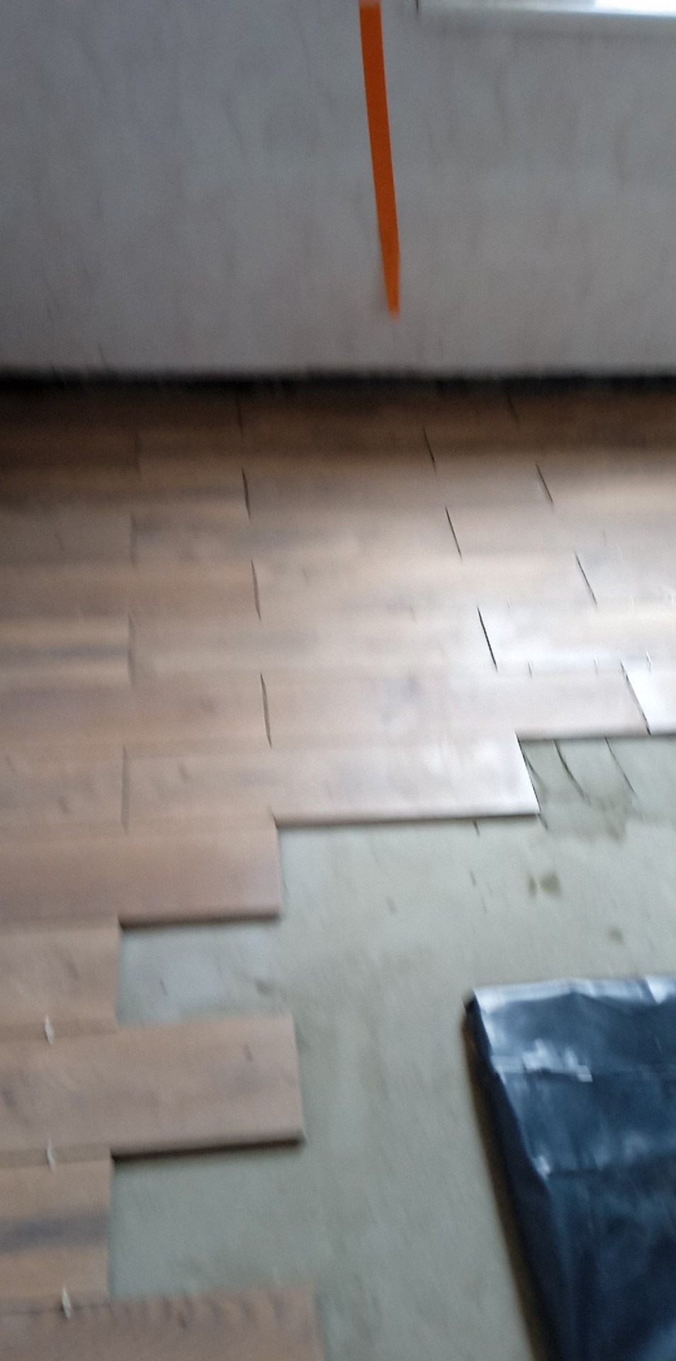 Układanie paneli podłogowych w trakcie pracy, widoczne listwy dystansowe i folia ochronna na podłodze, surowy stan wykończenia ścian i sufitu.