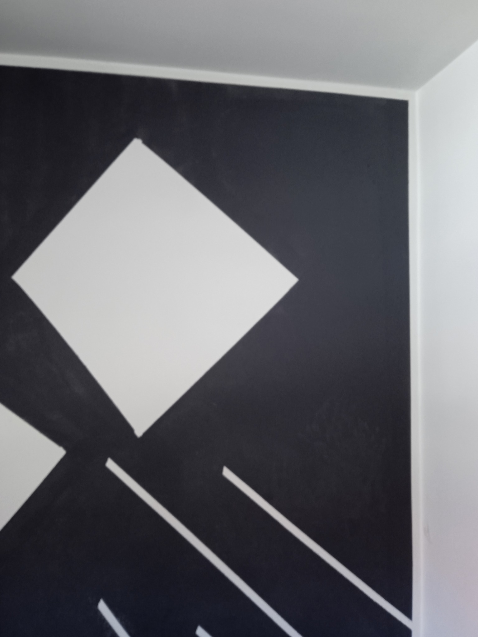 Czarno-biała ściana z geometrycznym wzorem, białe romby i ukośne linie na ciemnym tle, widok z bliska, fragment rogu ściany.