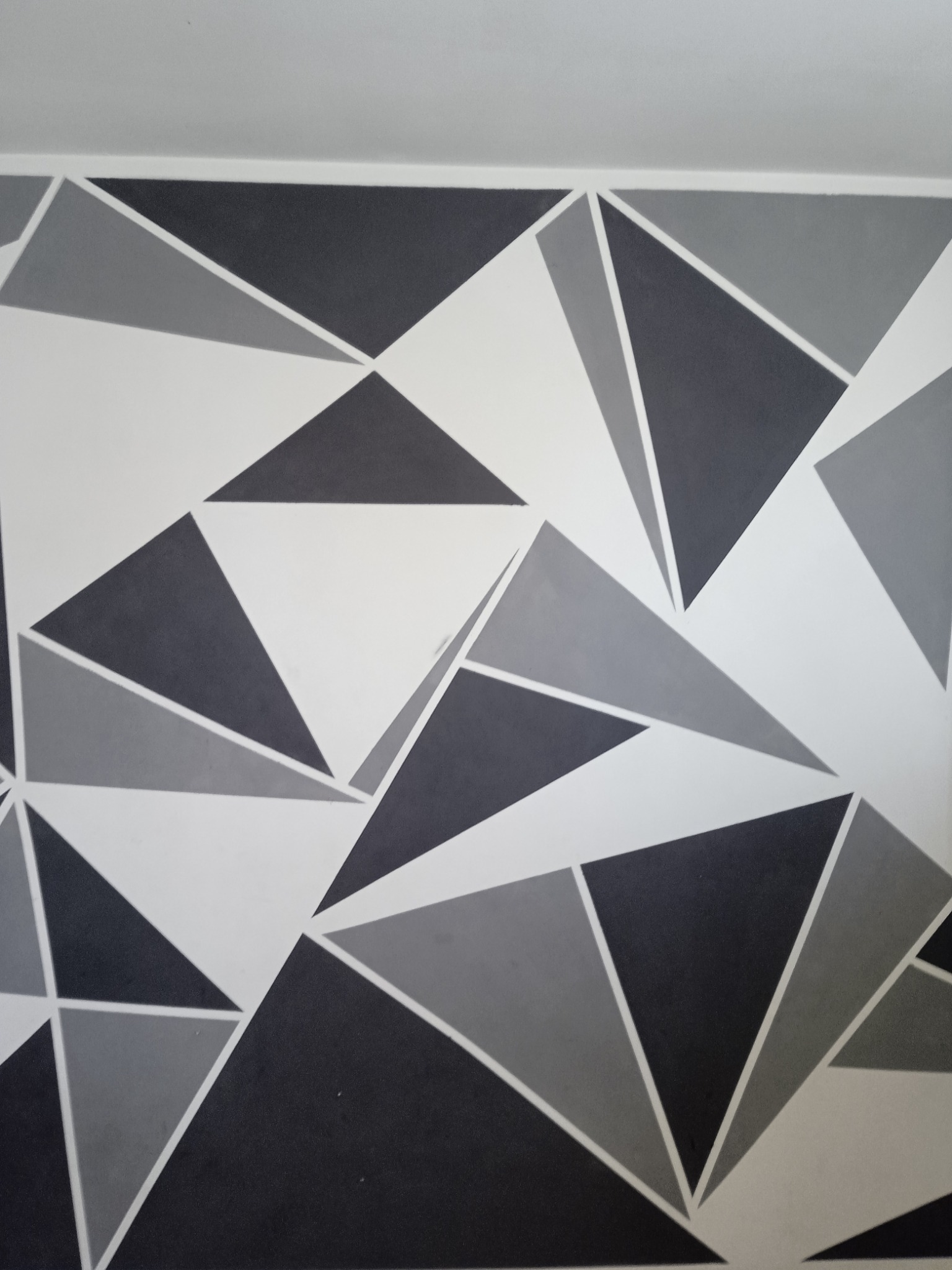 Ściana pomalowana w geometryczny wzór z trójkątów w odcieniach szarości i bieli, tworząca nowoczesny i dynamiczny efekt wizualny.