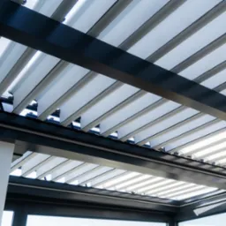 Nowoczesna pergola z metalową konstrukcją i regulowanymi lamelami, widok od dołu, z widocznymi oknami w tle.
