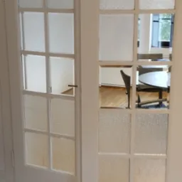 Białe, przeszklone drzwi wewnętrzne z otwartym skrzydłem, widoczny fragment parkietu i puszka z lakierem na podłodze.