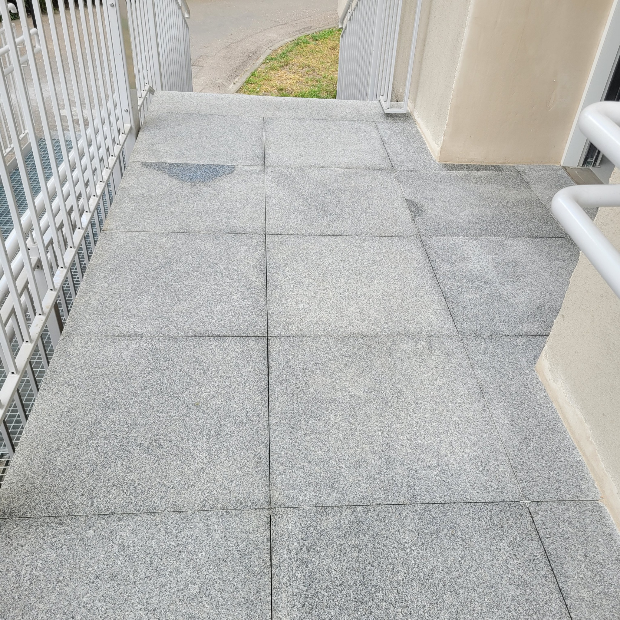 Granitowe płytki ułożone na schodach zewnętrznych z metalową barierką, widoczne ślady wilgoci.