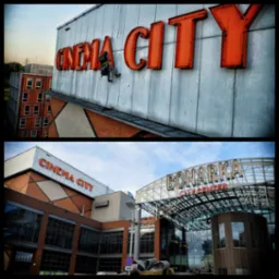 Pracownik na linach myje pomarańczowe litery 'CINEMA CITY' na wysokości, widok na budynek w tle.