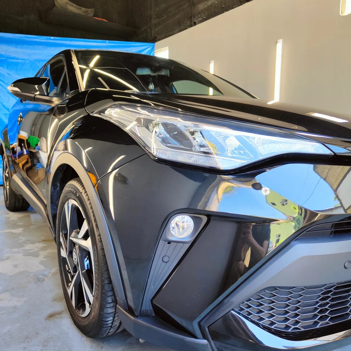 Błyszczący, czarny samochód Toyota C-HR po umyciu, widoczne odbicia w lakierze i detale przedniego grilla.