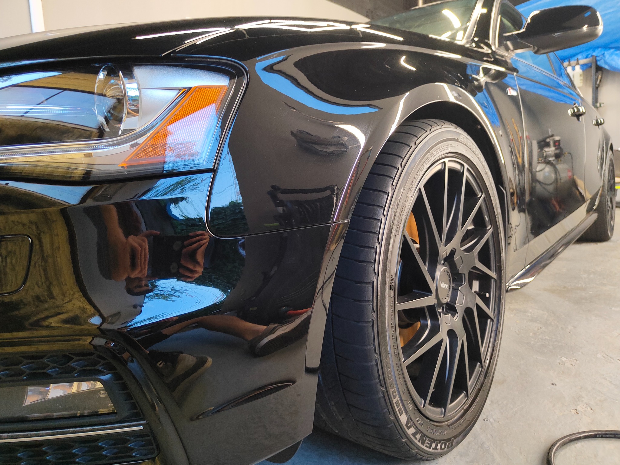 Błyszczący, czarny samochód po myciu w Rzeszowie, z widocznym odbiciem osoby robiącej zdjęcie na karoserii i detalami felg oraz opon.