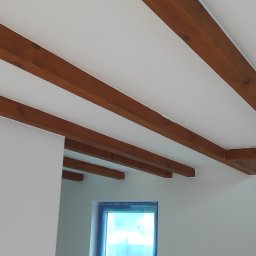 Vian - Wnętrze pokoju w trakcie malowania: białe ściany, drewniane belki stropowe, okno zabezpieczone folią malarską.