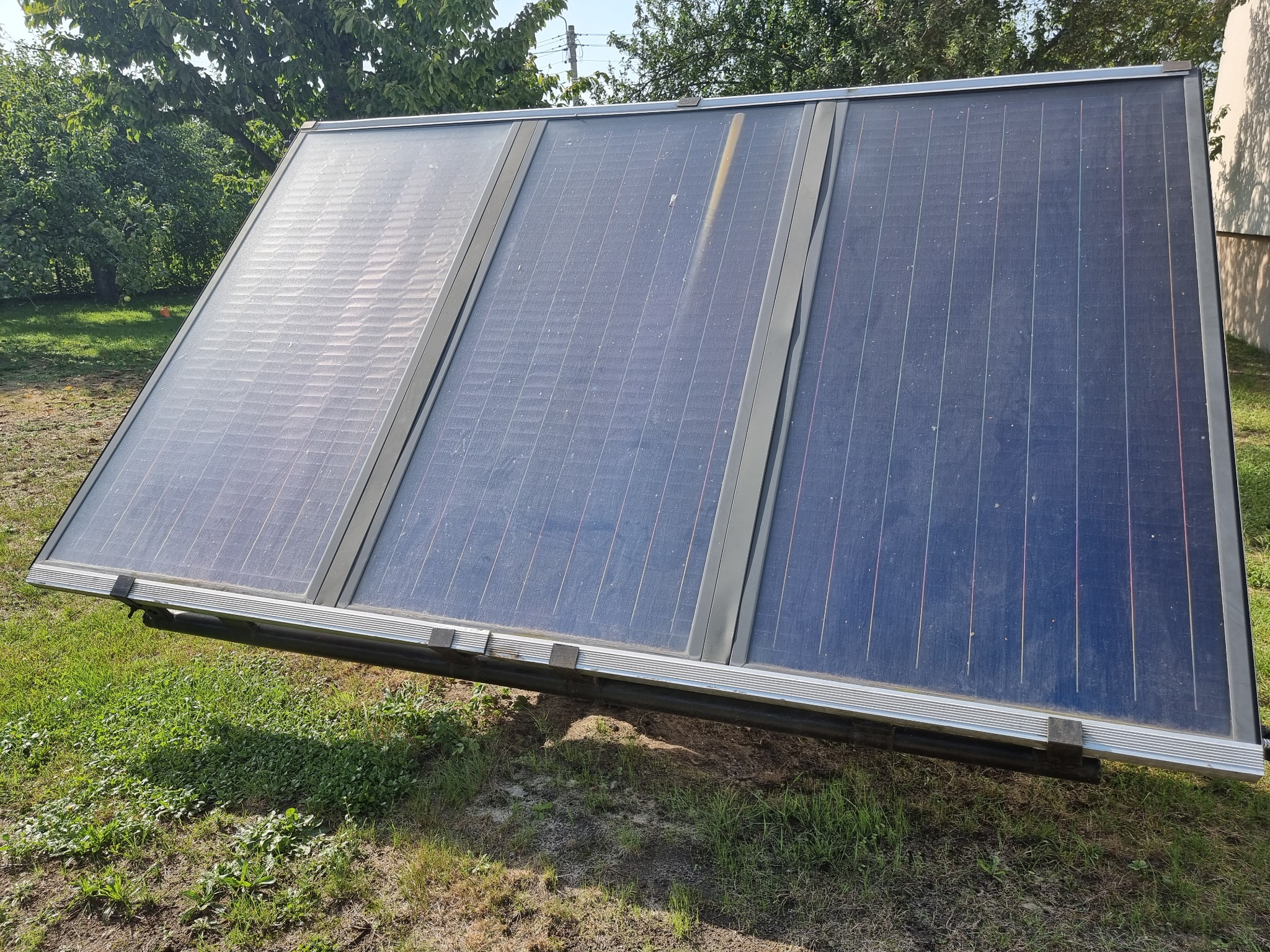 Trzyczęściowy panel solarny ustawiony na trawie, z widocznymi śladami użytkowania i elementami montażowymi.