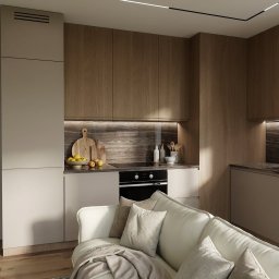 Łucja Orkisz Prim Area Studio - Nowoczesna kuchnia z drewnianymi szafkami i marmurowym blatem, widoczna z perspektywy salonu z białą sofą i beżowym pledem. Minimalistyczne oświetlenie sufitowe.