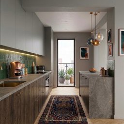 Łucja Orkisz Prim Area Studio - Wąska kuchnia z drewnianymi szafkami, zielonymi płytkami i dywanem w stylu vintage. Na blacie miedziany ekspres do kawy i toster. Balkon z roślinami w tle.