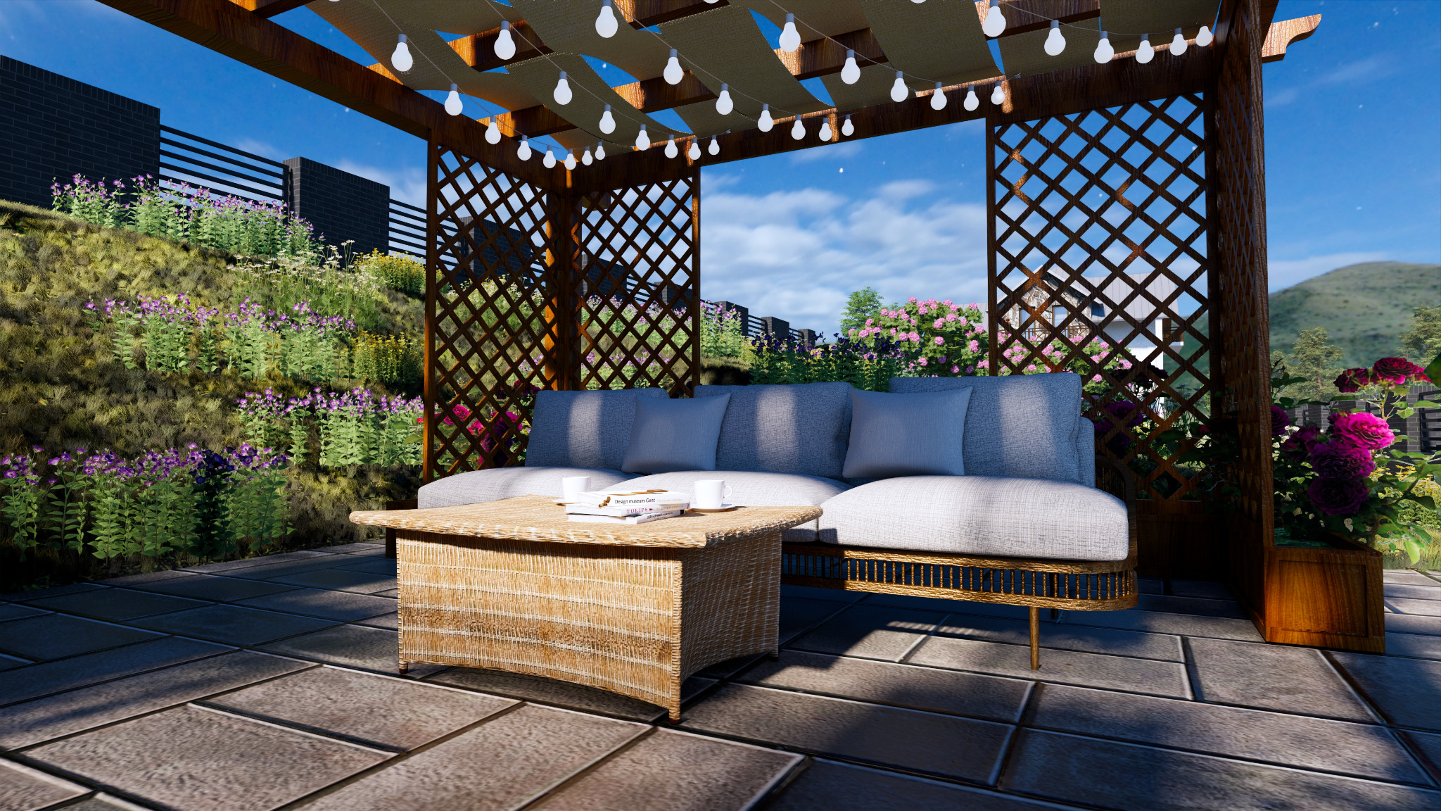 Zadaszony taras z wiklinowym stolikiem, szarą sofą z poduszkami i dekoracyjnymi lampkami, otoczony zielenią i kwiatami.