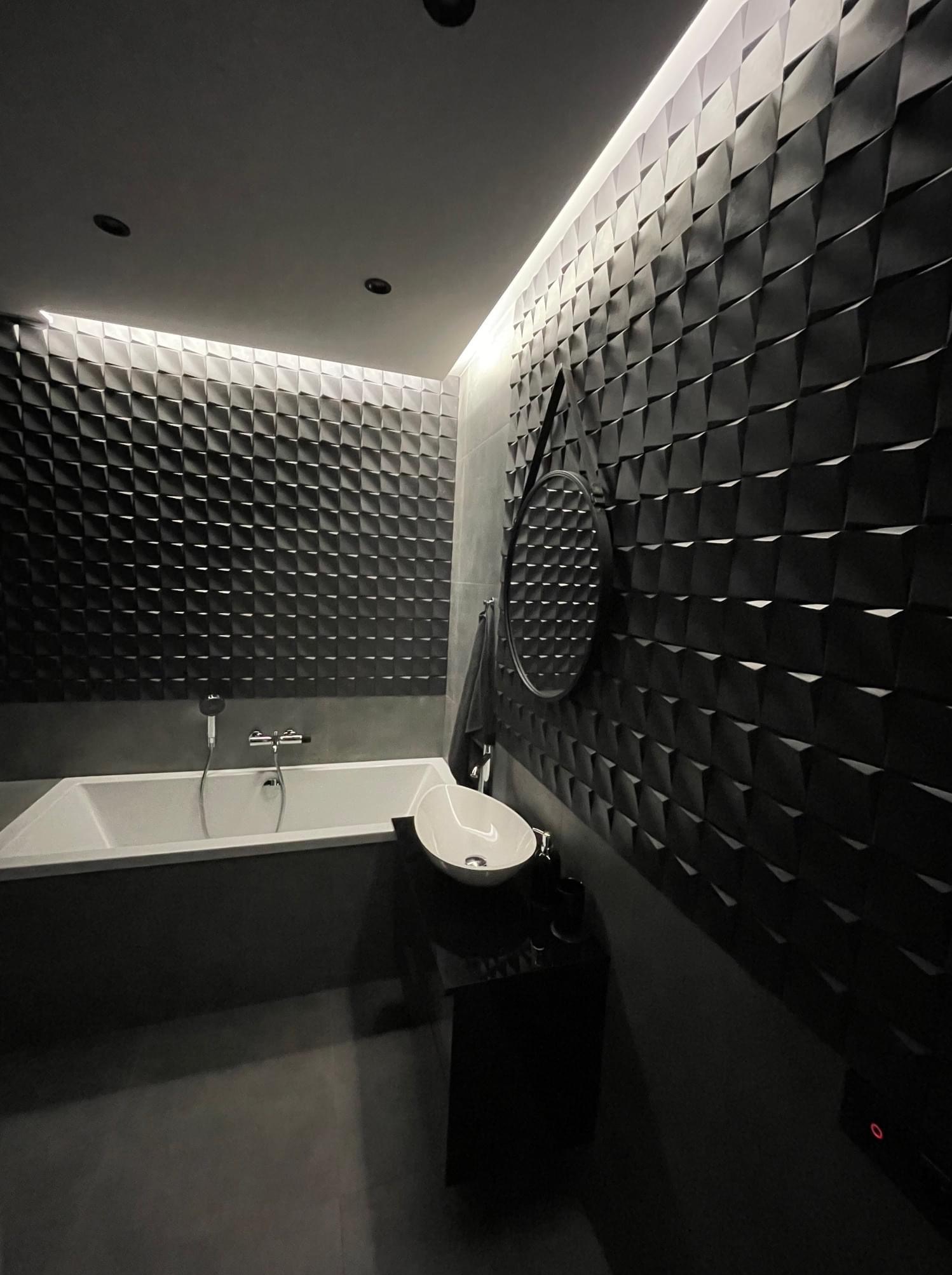Nowoczesna łazienka w odcieniach szarości i czerni z geometryczną ścianą 3D, podświetlanym sufitem, wolnostojącą umywalką i wanną.