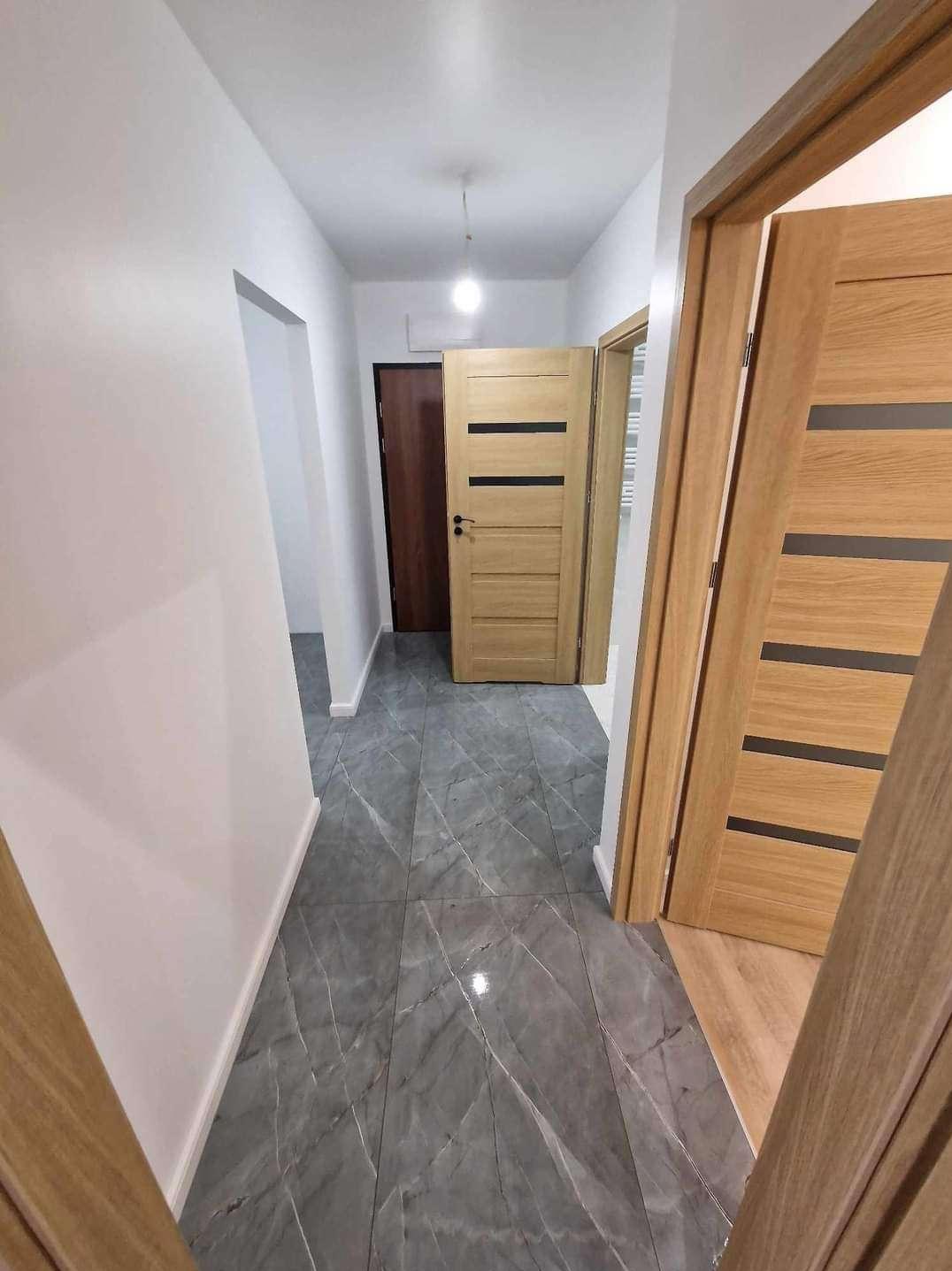 Korytarz po remoncie z szarymi płytkami imitującymi marmur na podłodze i trzema drewnianymi drzwiami z czarnymi wstawkami, widok z perspektywy wejścia.