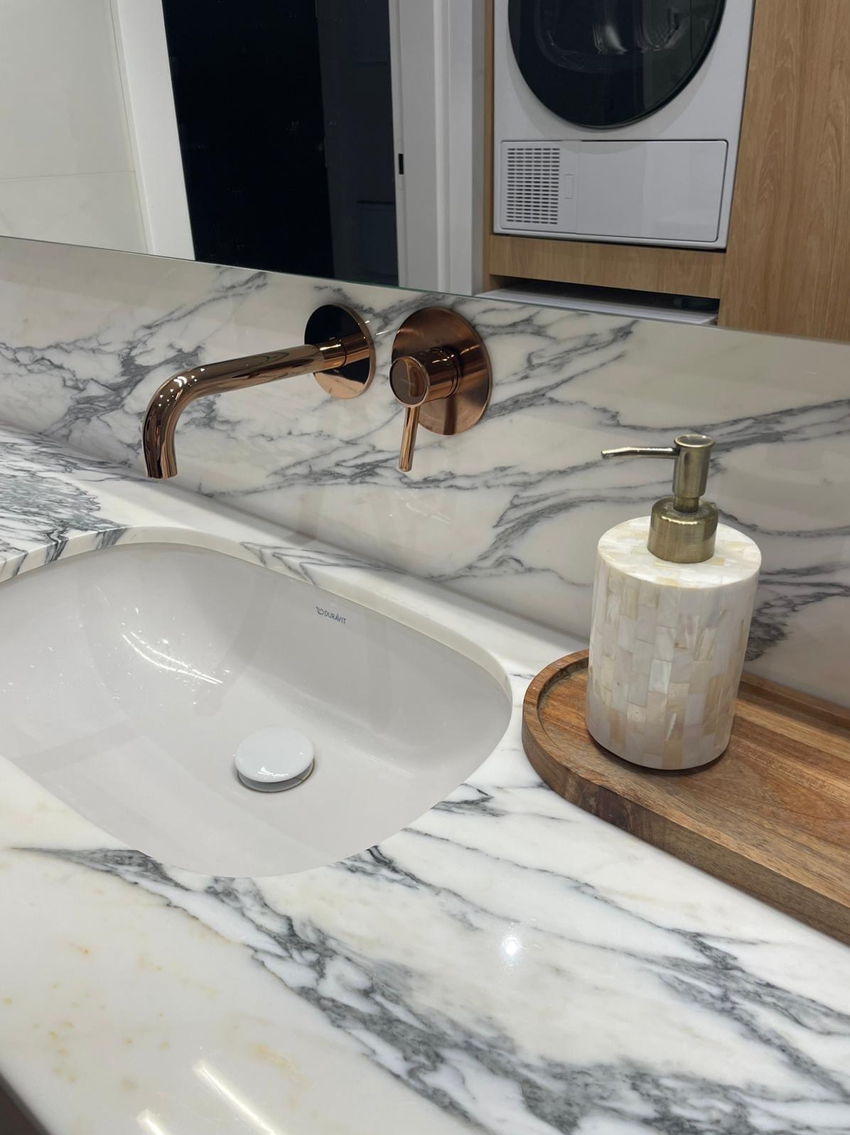 Nowoczesna łazienka z marmurowym blatem, umywalką Duravit, miedzianą armaturą ścienną i dozownikiem mydła z mozaiki perłowej na drewnianej tacy.