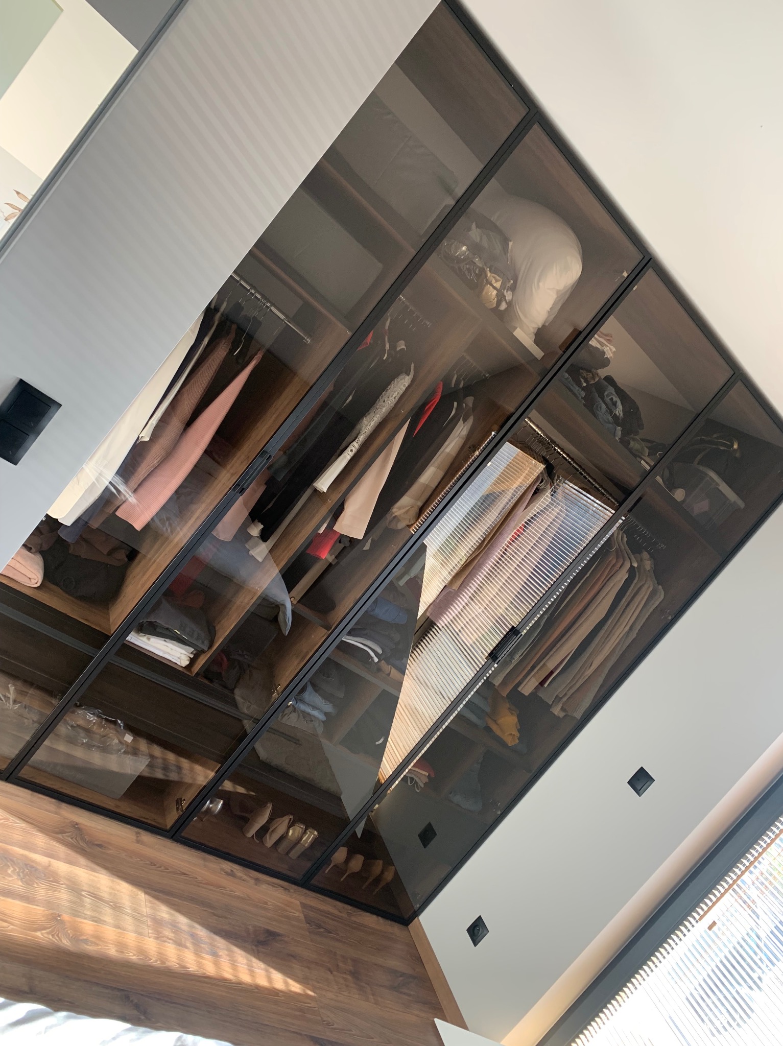 Szklana szafa wnękowa z ciemnymi ramami, widok na ubrania i akcesoria w środku, poddasze.