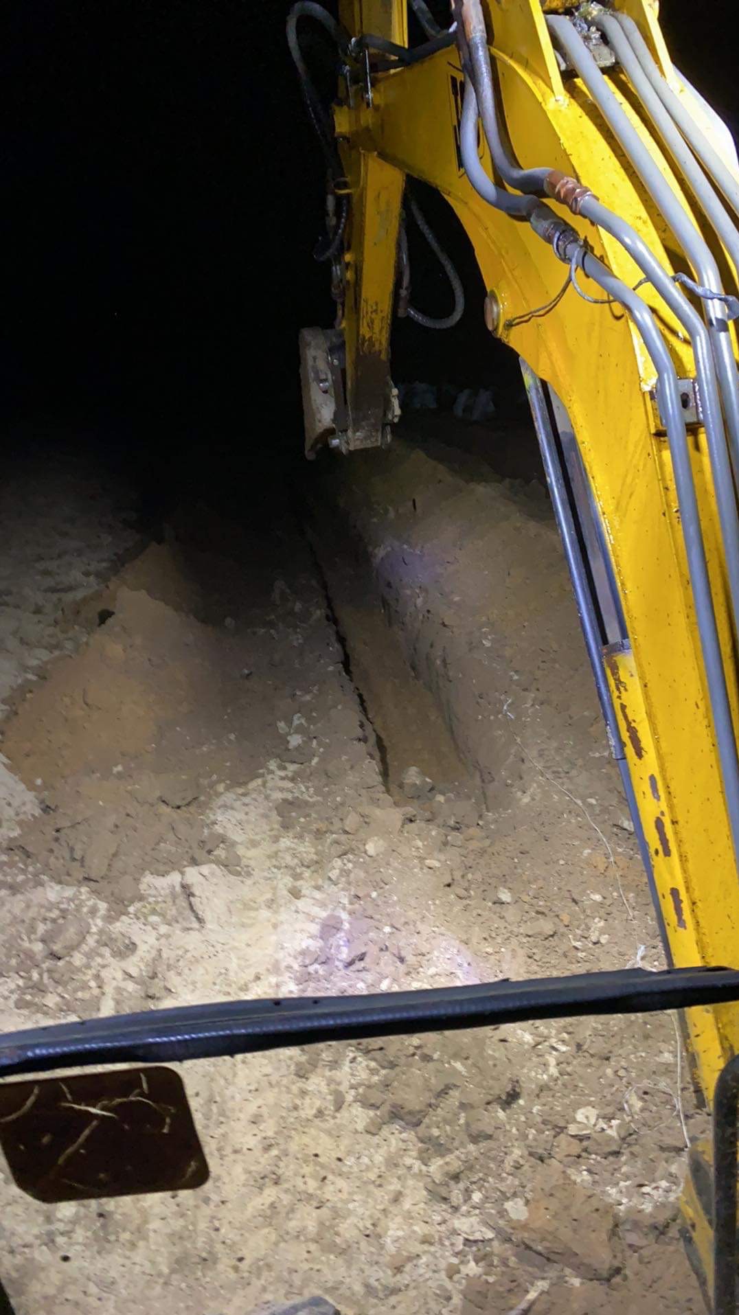 Żółty wysięgnik koparki zagłębia się w ziemię, tworząc głęboki wykop w ciemności, oświetlony jedynie reflektorami maszyny.