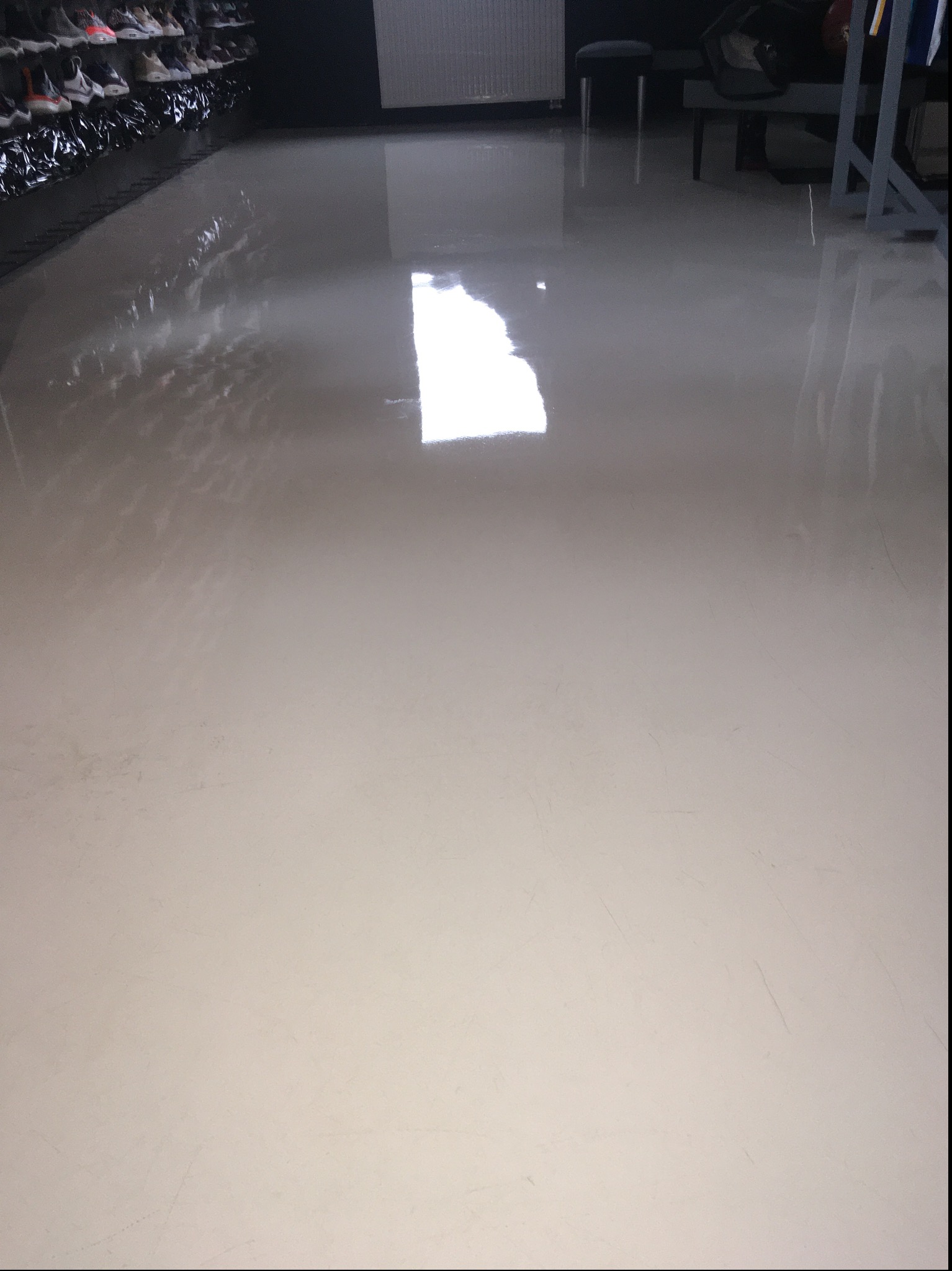 Błyszcząca, świeżo umyta podłoga w sklepie obuwniczym, z odbiciami światła i rzędami butów na półkach w tle.