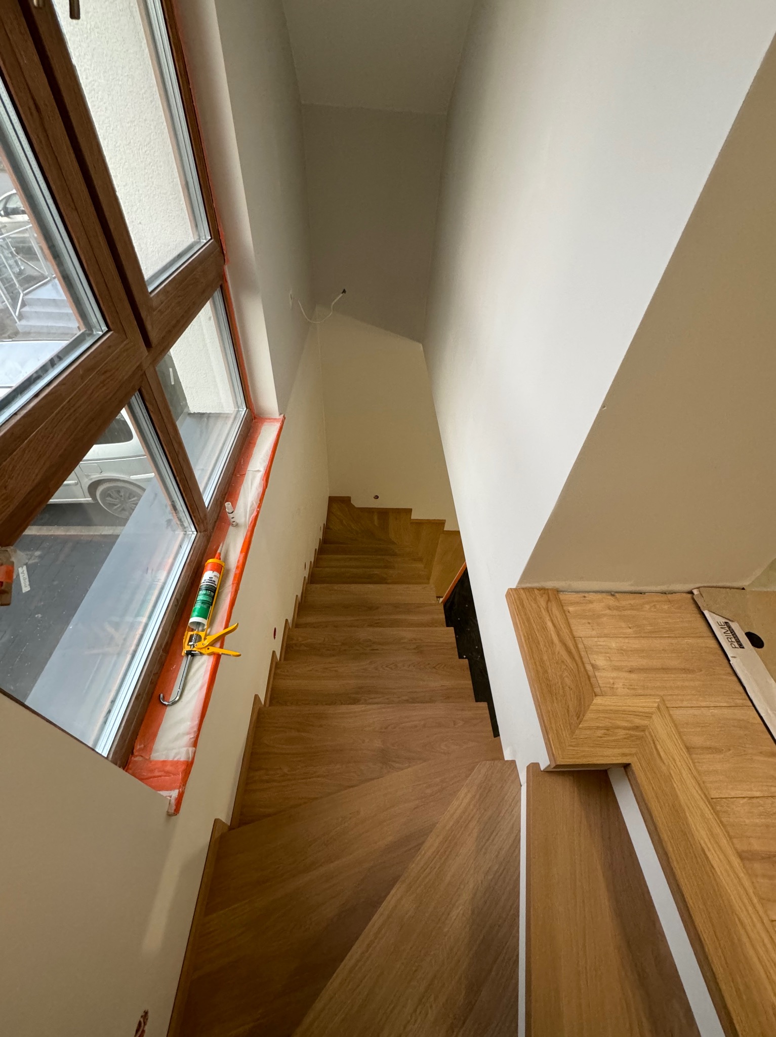 Montaż drewnianych schodów z widocznym oknem i aplikatorem silikonu, etap wykończeniowy.