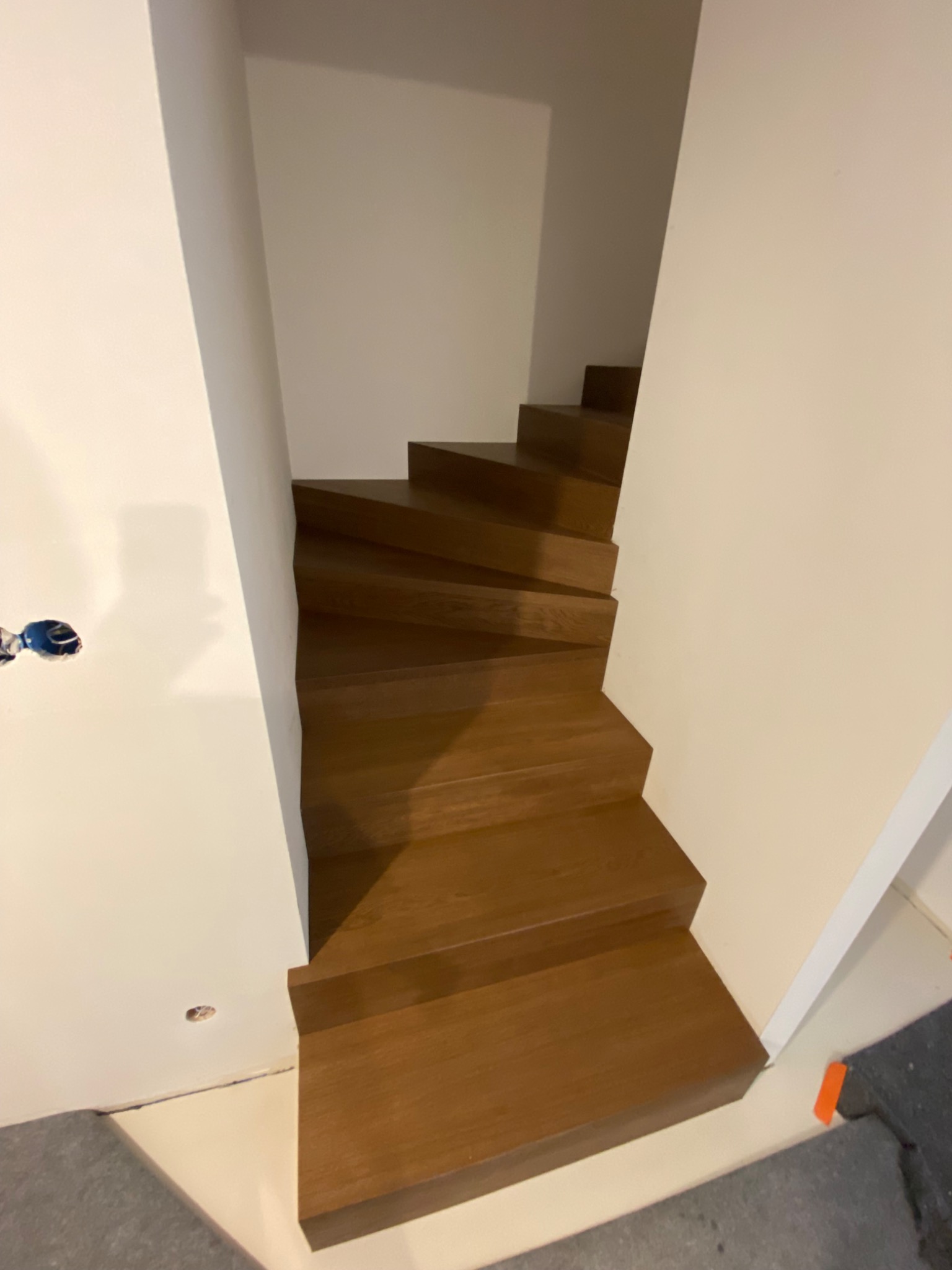 Wewnętrzne schody z ciemnego drewna, bez poręczy, w nowym domu, widoczne niedokończone prace wykończeniowe.