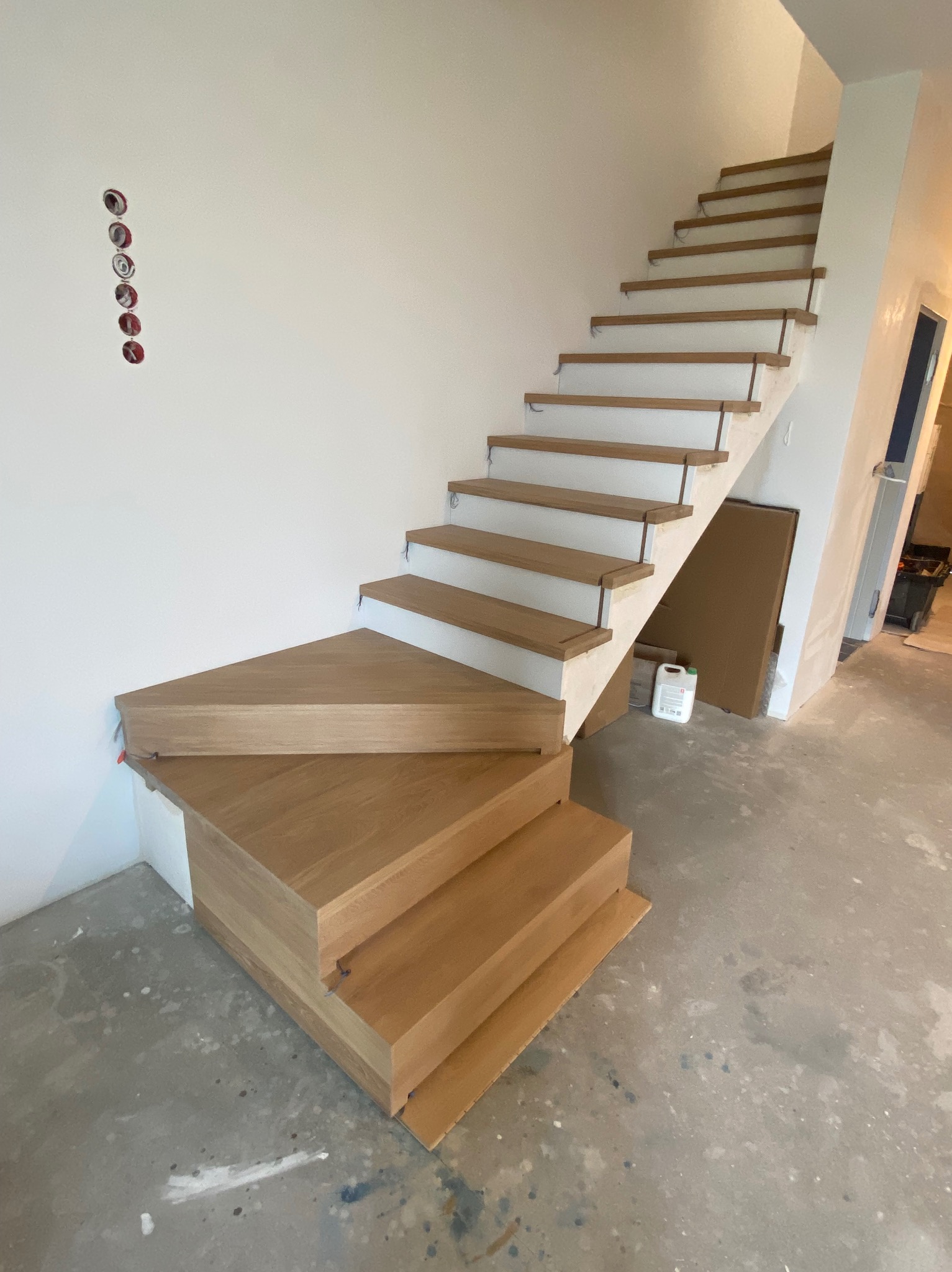 Montaż drewnianych schodów wewnętrznych z białymi podstopnicami, widoczne niedokończone wykończenie i wystające przewody elektryczne w ścianie.