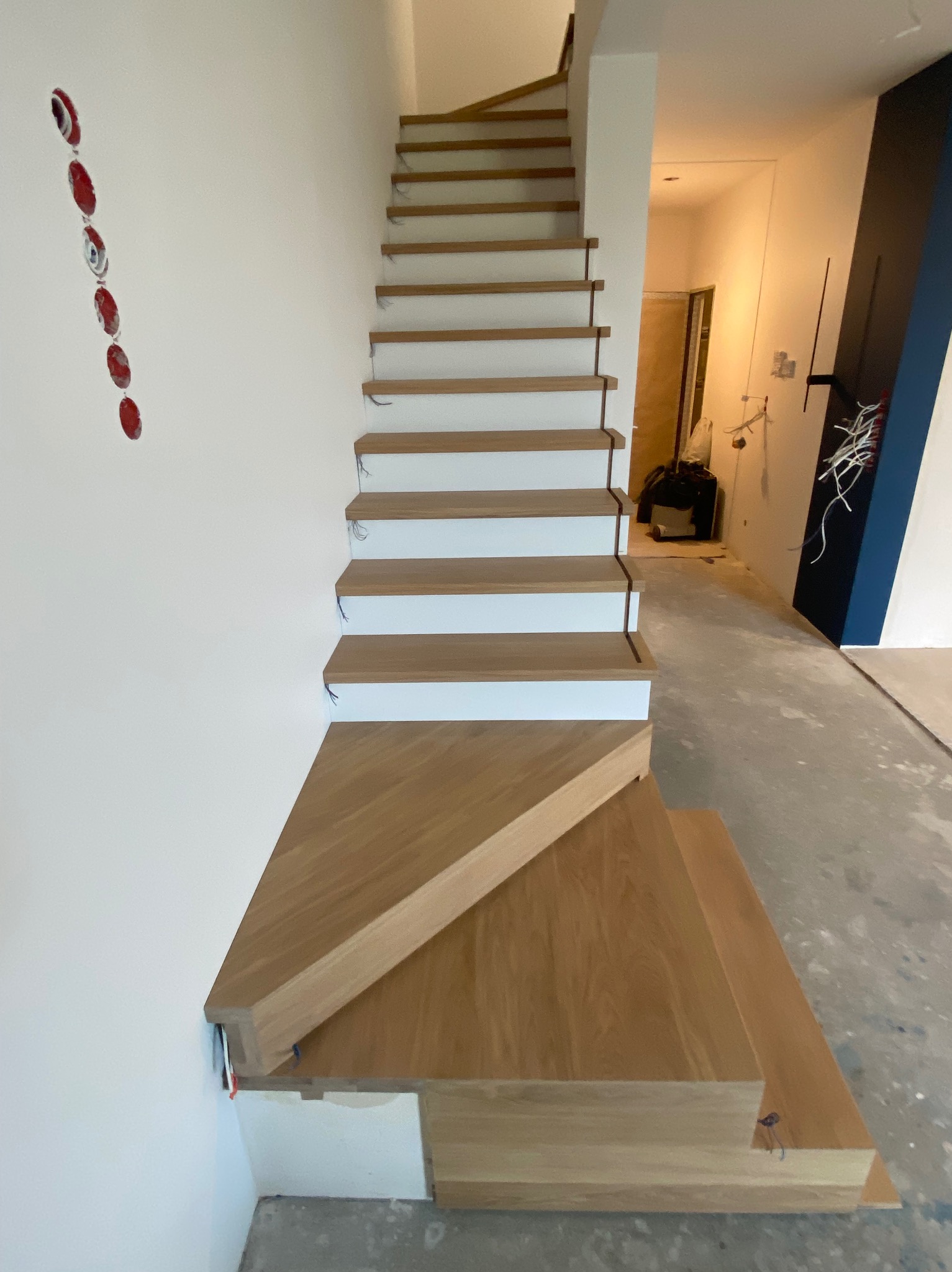 Wewnętrzne schody z drewnianymi stopniami i białymi podstopnicami, widoczne kable elektryczne w ścianie i niedokończone wykończenie podłogi.