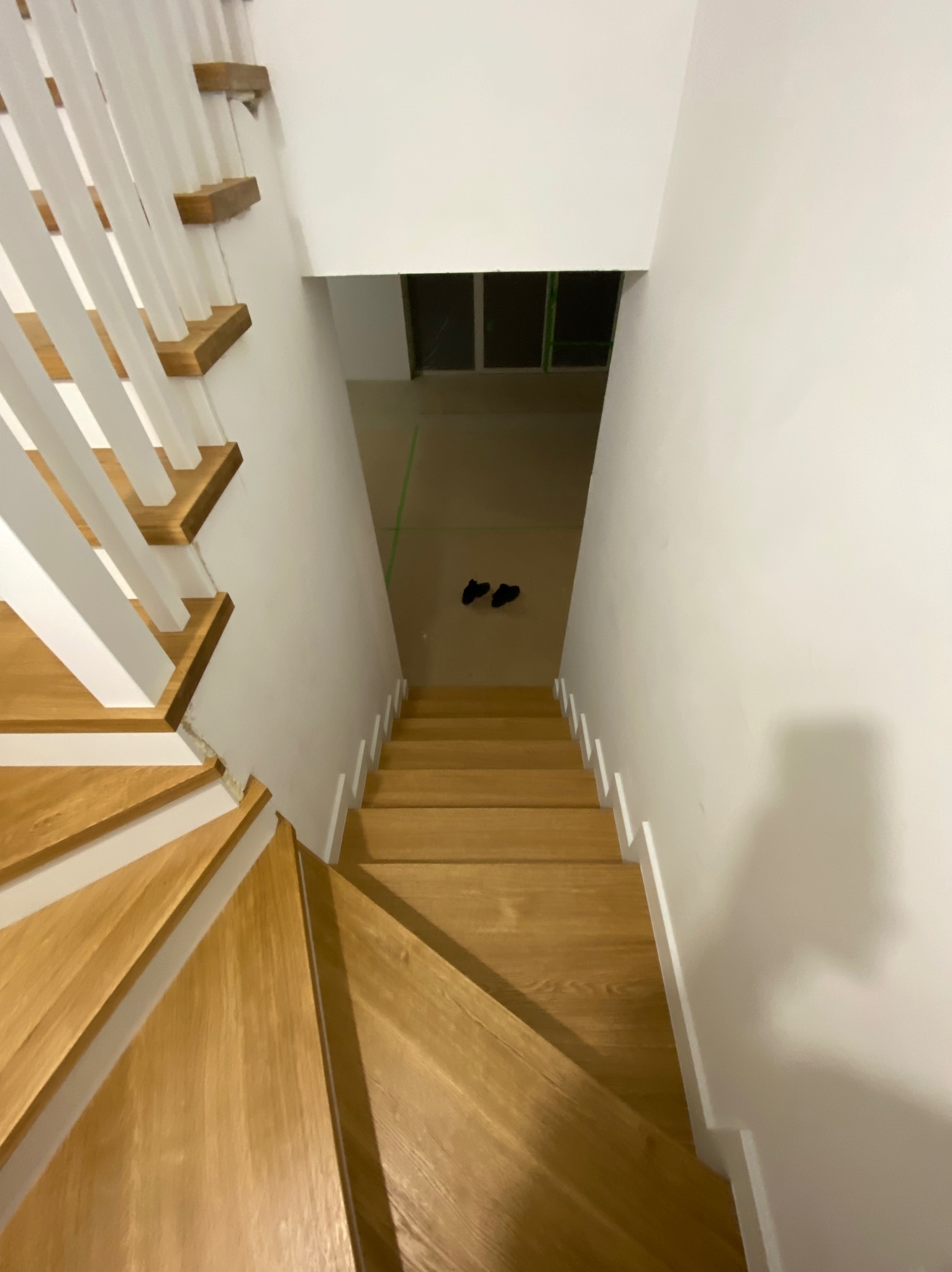 Widok z góry na drewniane schody z białymi poręczami w trakcie montażu, z widocznymi butami na podłodze w tle.