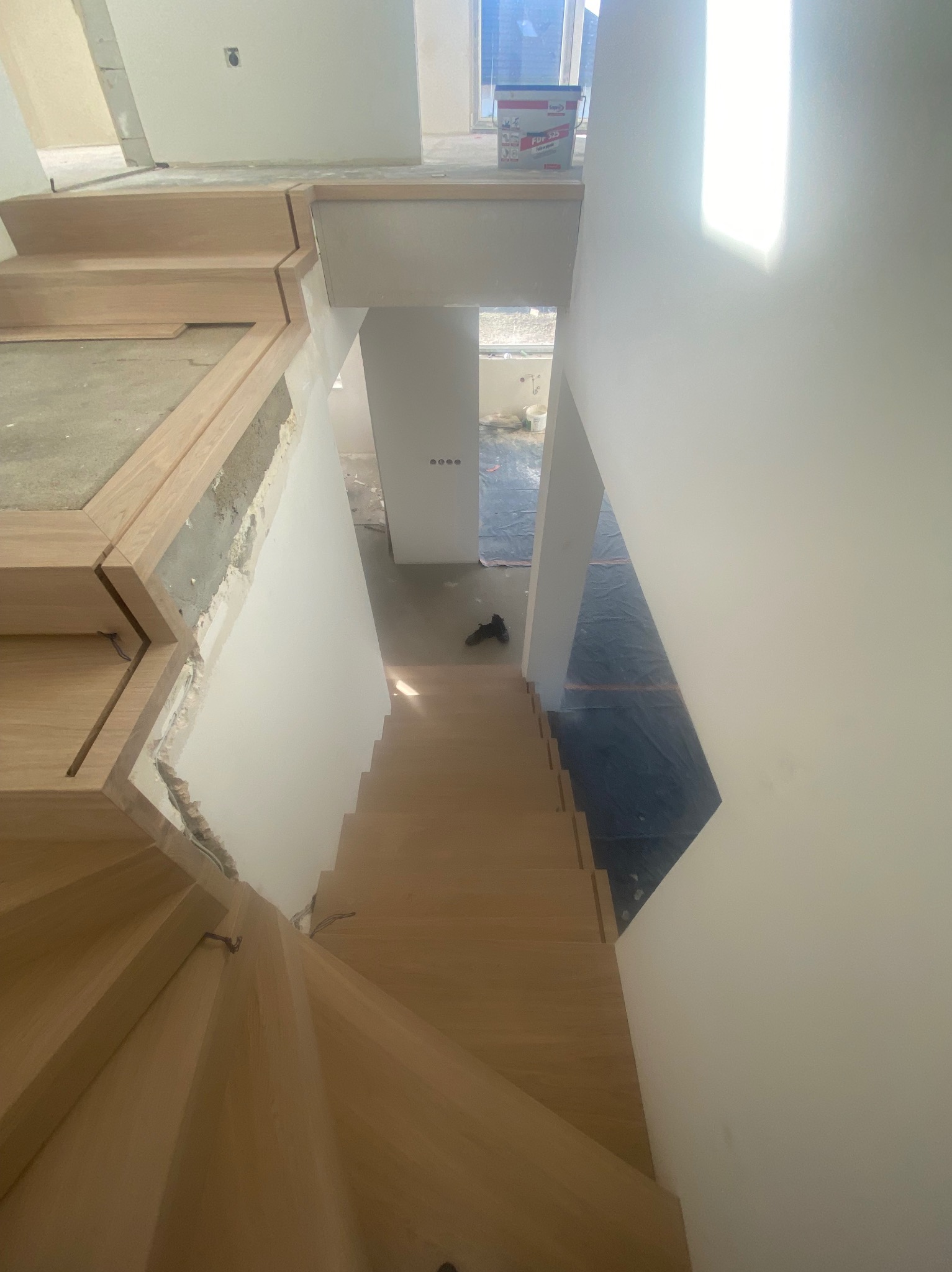 Wewnętrzne schody z surowego drewna w trakcie montażu, widoczne niedoskonałości wykończenia ścian i brakujące listwy przypodłogowe, perspektywa z góry.