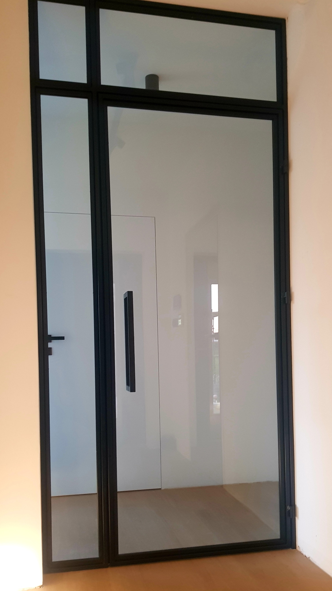 Nowoczesne drzwi wewnętrzne ze szkła w czarnej ramie, widok z boku, zarys drugiego pomieszczenia w odbiciu szyby.