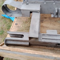 Soda trix - Szary, metalowy element konstrukcyjny, prawdopodobnie fragment maszyny, leżący na drewnianej skrzyni, po obróbce ściernej.