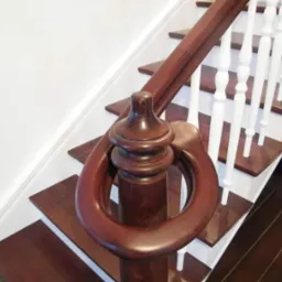 Detale wykończenia drewnianych schodów z ciemnego drewna z białą balustradą, widoczny ozdobny element poręczy w kształcie łzy.