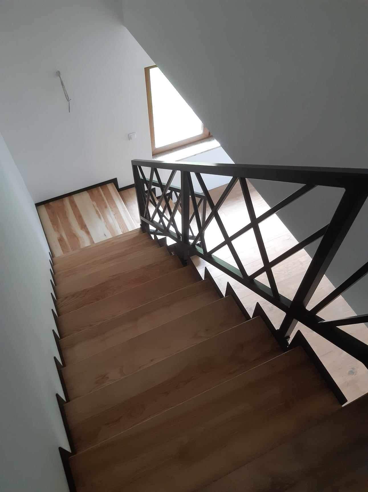 Wnętrze domu ze schodami z jasnego drewna i nowoczesną, geometryczną balustradą w kolorze ciemnego grafitu, widziane z góry.