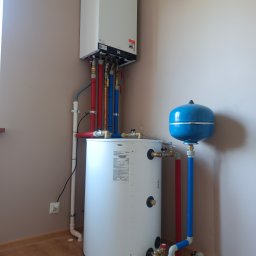 Eko Serwis - Biały piec gazowy kondensacyjny Viessmann z podłączonym zasobnikiem ciepłej wody i niebieskim naczyniem przeponowym, instalacja w rogu pomieszczenia.
