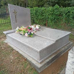 AD GRANIT Adrian Biega - Granitowy nagrobek z krzyżem i kwiatami, otoczony zielenią, widok z boku.