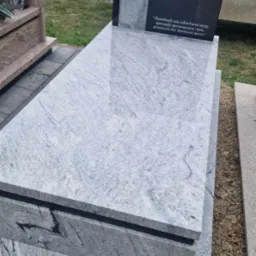 Nowoczesny nagrobek z jasnoszarego granitu z ciemnymi akcentami i wyrytym epitafium, ustawiony na cmentarzu